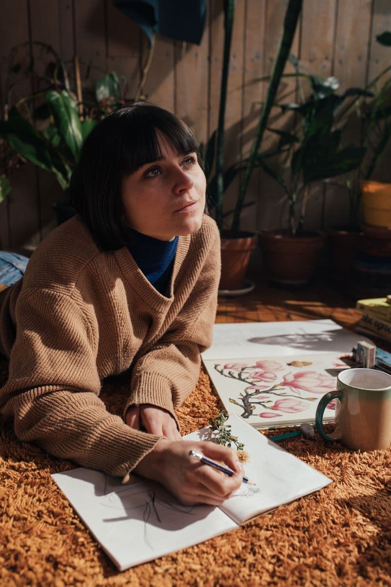 Aoife Devlin sketching botanicals on a warm rust rug, plants around her