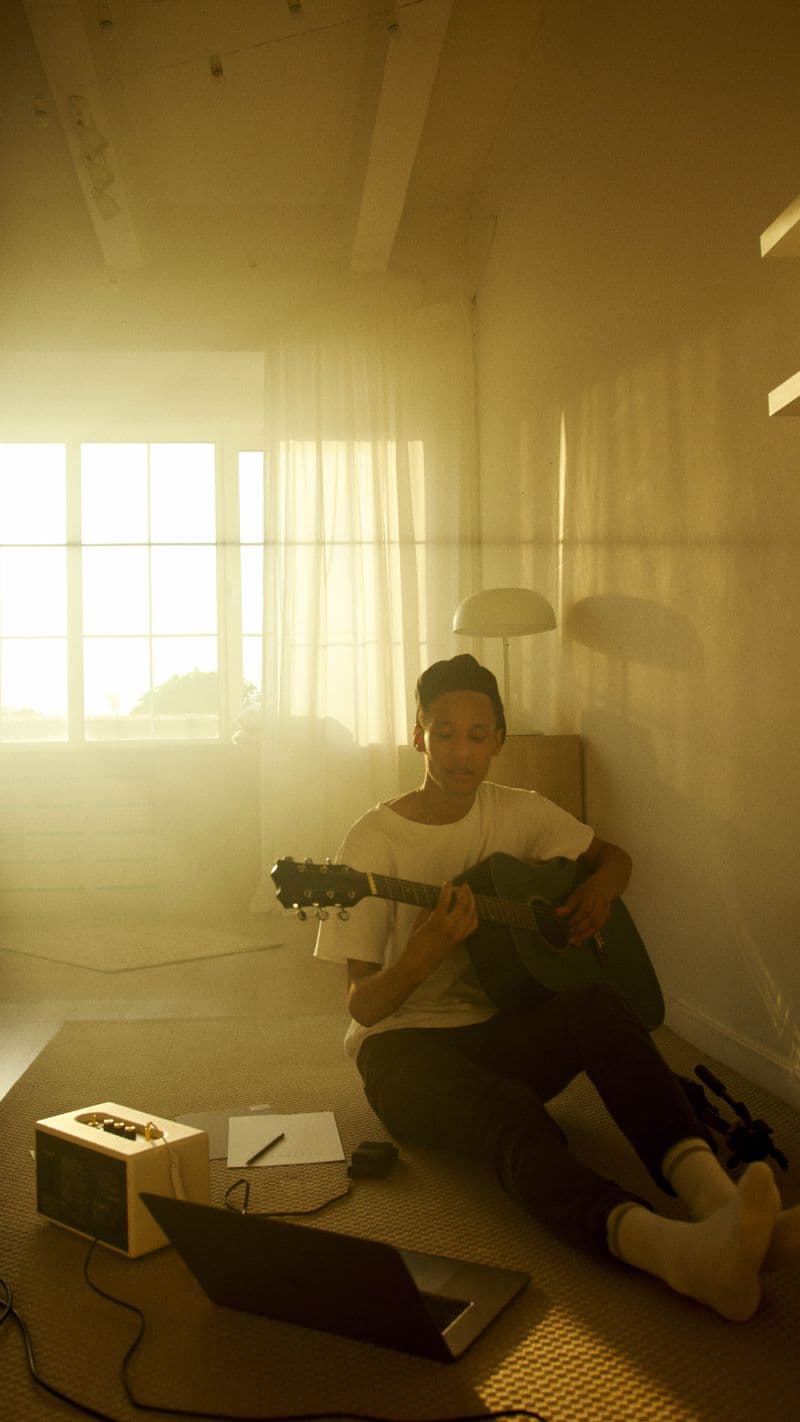 Kai Otieno at home, guitar on his lap in golden-hour light